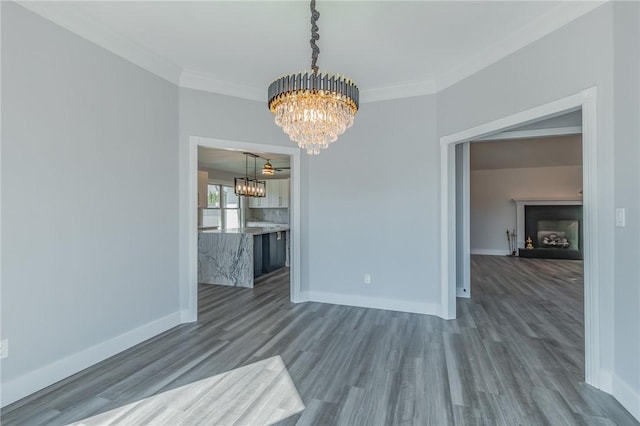 unfurnished dining area featuring dark wood finished floors, crown molding, baseboards, and a chandelier