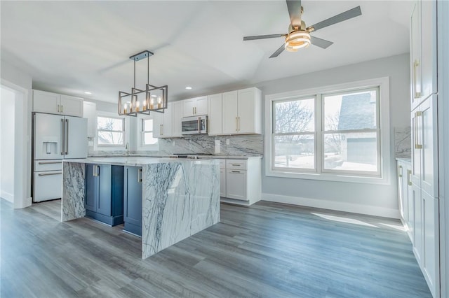 kitchen featuring high end white refrigerator, stainless steel microwave, white cabinets, and backsplash