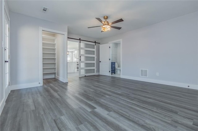 unfurnished bedroom featuring a barn door, wood finished floors, visible vents, and baseboards