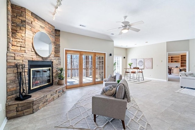 living area featuring visible vents, baseboards, a stone fireplace, french doors, and a ceiling fan