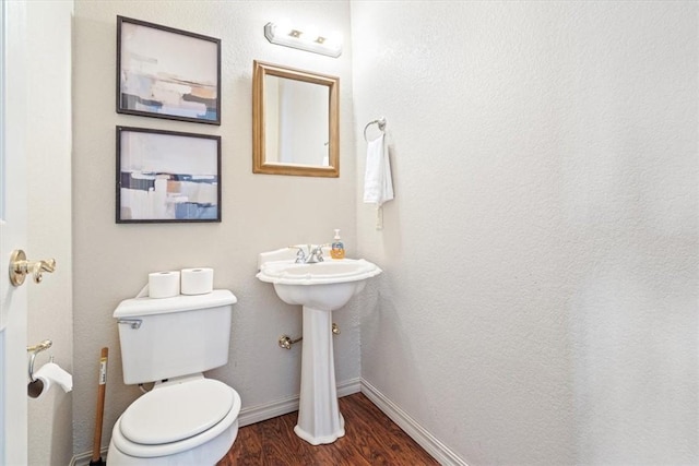 half bathroom featuring toilet, wood finished floors, and baseboards