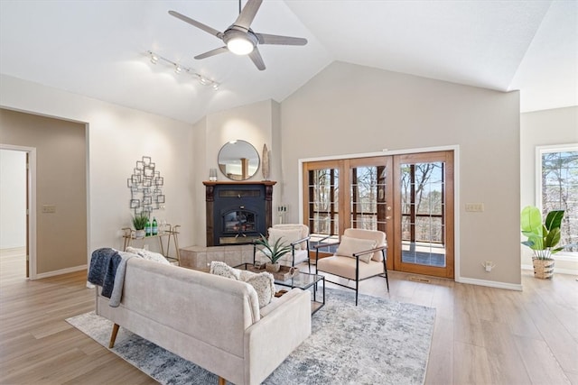 living room with a tiled fireplace, baseboards, light wood-style floors, and vaulted ceiling