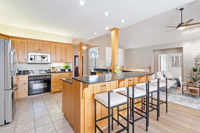 kitchen featuring open floor plan, a breakfast bar, lofted ceiling, decorative columns, and stainless steel appliances