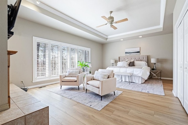 bedroom featuring visible vents, light wood-type flooring, a raised ceiling, and baseboards