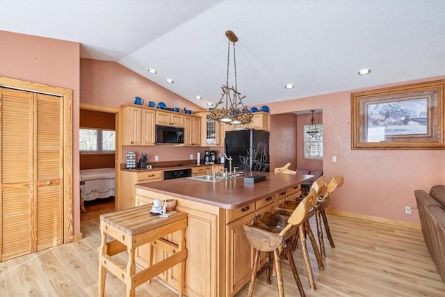 kitchen featuring a kitchen bar, black appliances, vaulted ceiling, and a sink