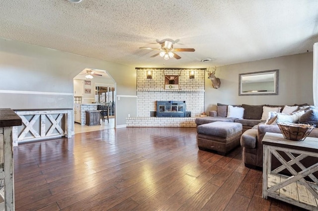 living room with hardwood / wood-style floors, a ceiling fan, a fireplace, arched walkways, and a textured ceiling