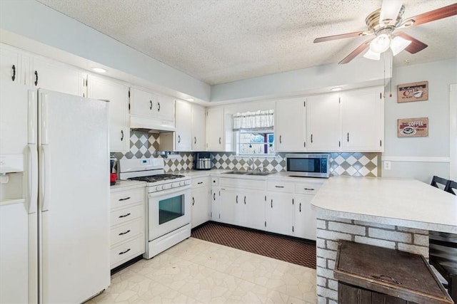 kitchen with a sink, under cabinet range hood, white appliances, white cabinets, and light countertops