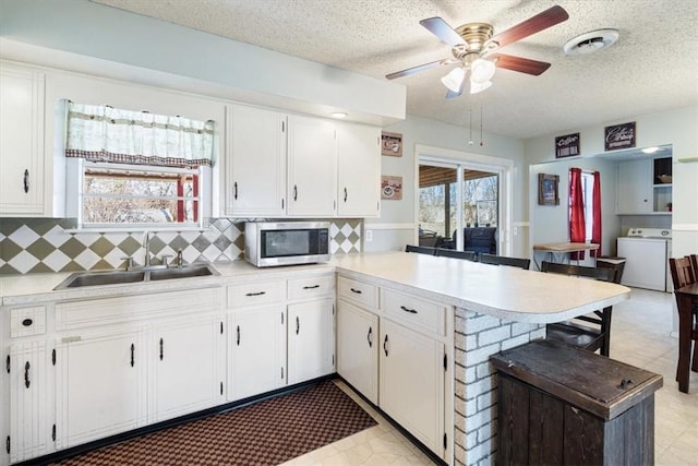 kitchen featuring a sink, stainless steel microwave, washer / clothes dryer, a peninsula, and light countertops