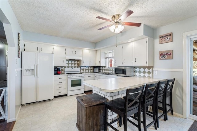 kitchen with white appliances, a peninsula, light countertops, under cabinet range hood, and white cabinetry