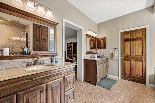 bathroom with a tile shower, two vanities, baseboards, and a sink