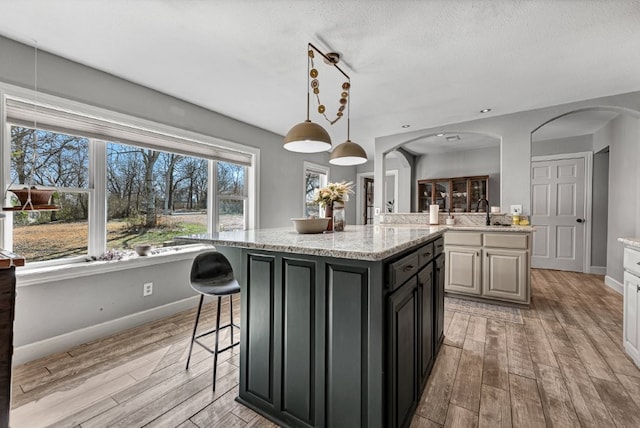 kitchen with arched walkways, light wood finished floors, a breakfast bar area, and a sink