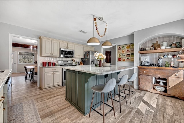 kitchen featuring visible vents, light wood finished floors, stainless steel appliances, decorative backsplash, and cream cabinets