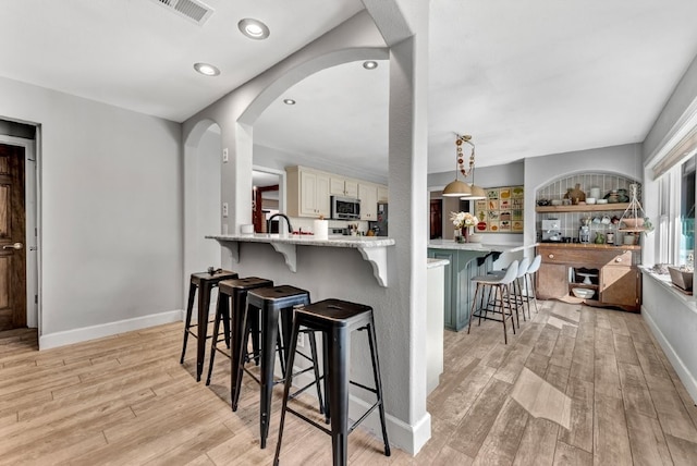 kitchen featuring a kitchen bar, stainless steel microwave, light wood-style floors, and visible vents