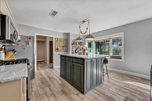 kitchen with visible vents, light wood-style flooring, appliances with stainless steel finishes, and a breakfast bar area