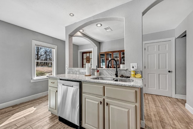 kitchen featuring visible vents, dishwasher, light wood-style floors, arched walkways, and a sink