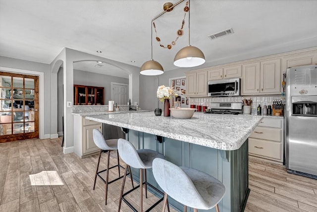 kitchen featuring visible vents, backsplash, appliances with stainless steel finishes, a kitchen breakfast bar, and light wood-style floors