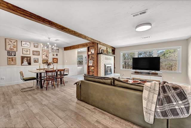 living room with visible vents, a brick fireplace, beamed ceiling, wainscoting, and wood finished floors