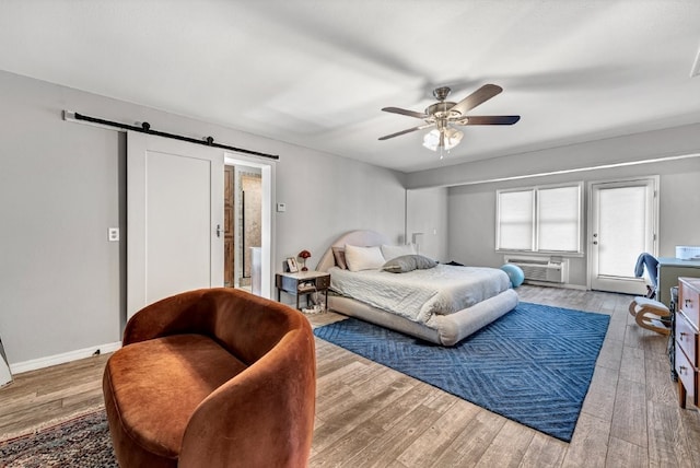 bedroom featuring a barn door, baseboards, wood finished floors, and access to exterior