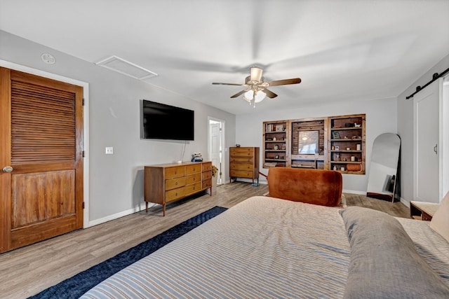 bedroom featuring a ceiling fan, a barn door, wood finished floors, and baseboards