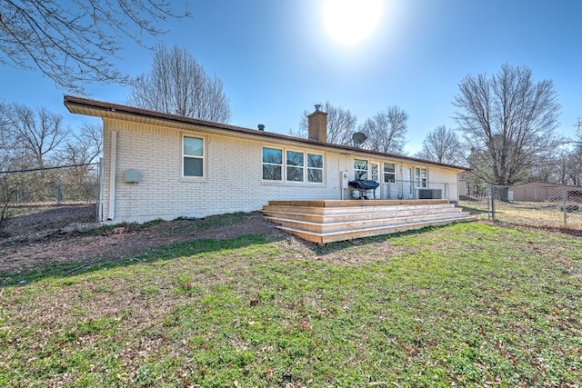 rear view of house with brick siding, a chimney, a yard, and fence