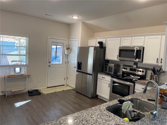 kitchen featuring wood finished floors, visible vents, dark stone counters, a sink, and stainless steel appliances