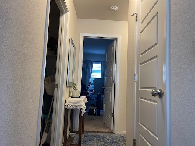 hallway featuring dark carpet and a textured wall