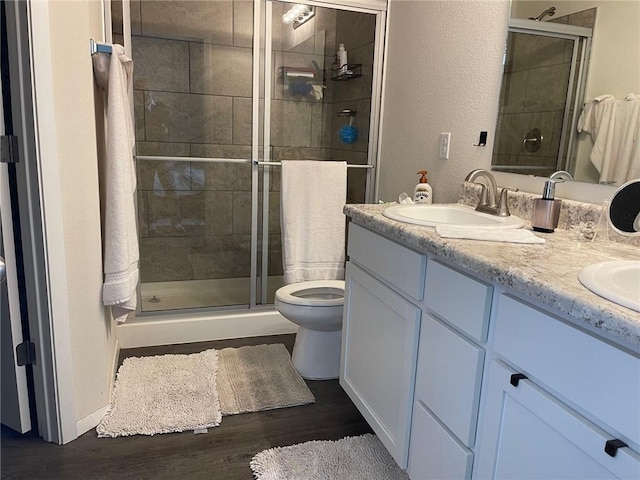 bathroom featuring toilet, double vanity, a stall shower, wood finished floors, and a sink