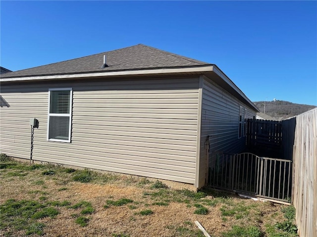 view of side of home with a shingled roof and fence