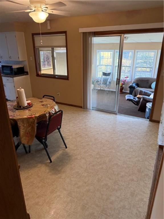 dining space with baseboards, light floors, and a ceiling fan