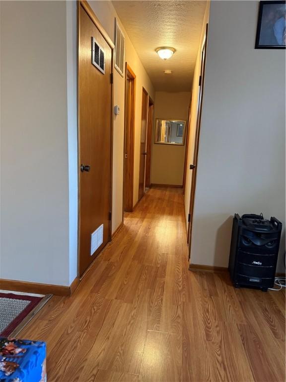 corridor with visible vents, a textured ceiling, light wood-type flooring, and baseboards