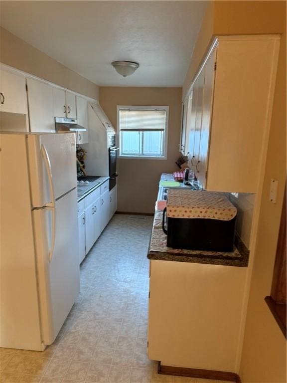 kitchen featuring dark countertops, under cabinet range hood, light floors, freestanding refrigerator, and white cabinets