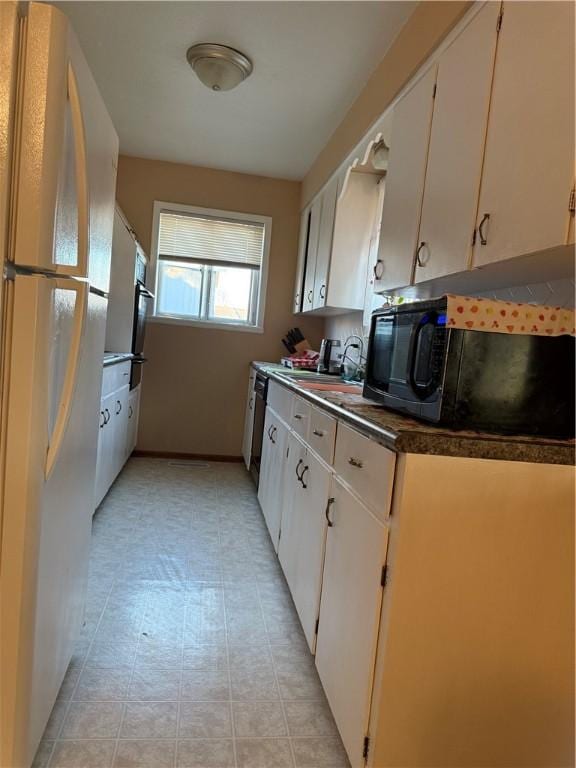 kitchen with a sink, dark countertops, freestanding refrigerator, white cabinets, and black microwave