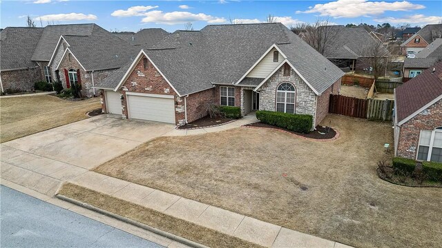 view of front of house with fence, driveway, an attached garage, a shingled roof, and brick siding