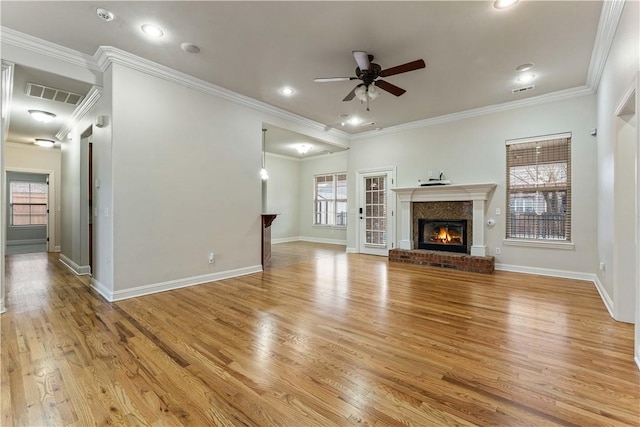 unfurnished living room with visible vents, light wood-style floors, crown molding, a brick fireplace, and ceiling fan