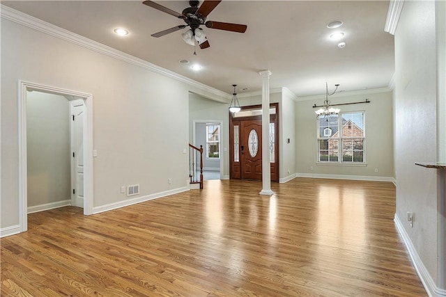 foyer entrance with visible vents, light wood-style flooring, ornamental molding, ceiling fan with notable chandelier, and ornate columns