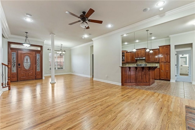 interior space with decorative columns, light wood-style floors, ornamental molding, and ceiling fan with notable chandelier