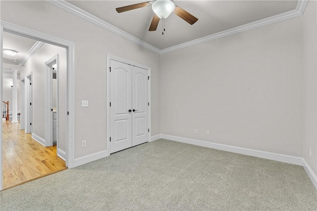 unfurnished bedroom with a closet, carpet floors, crown molding, baseboards, and ceiling fan