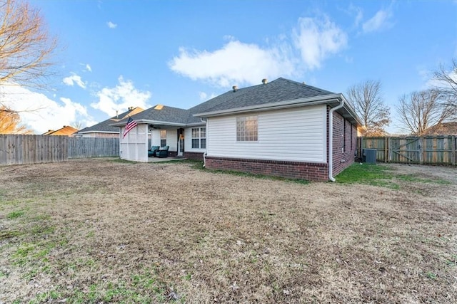 rear view of property featuring a yard, central AC unit, a fenced backyard, and roof with shingles