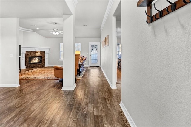 entrance foyer featuring baseboards, dark wood finished floors, ornamental molding, a premium fireplace, and a ceiling fan