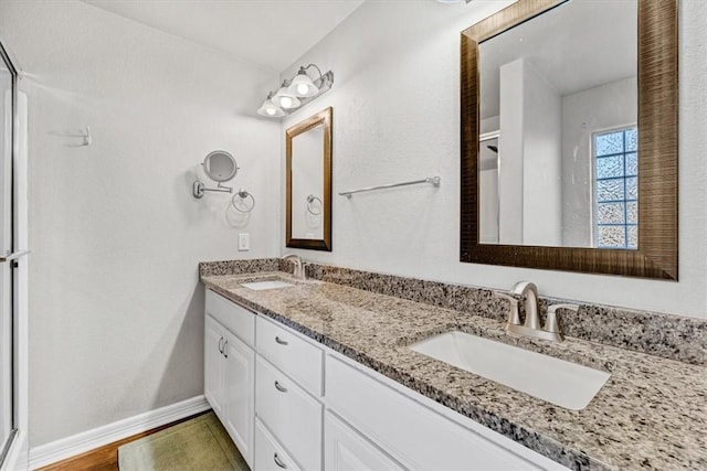 full bath with double vanity, wood finished floors, baseboards, and a sink