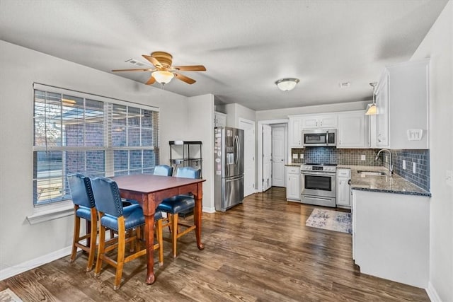 kitchen with dark wood-style floors, a sink, stainless steel appliances, white cabinets, and backsplash