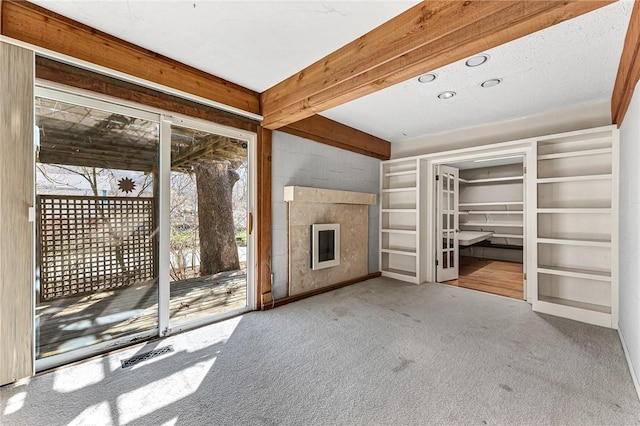 unfurnished living room featuring a glass covered fireplace, beam ceiling, carpet, and visible vents