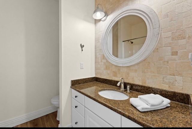 bathroom with toilet, tasteful backsplash, wood finished floors, baseboards, and vanity