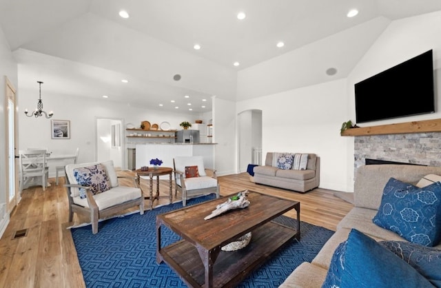 living room featuring visible vents, wood finished floors, arched walkways, a fireplace, and lofted ceiling