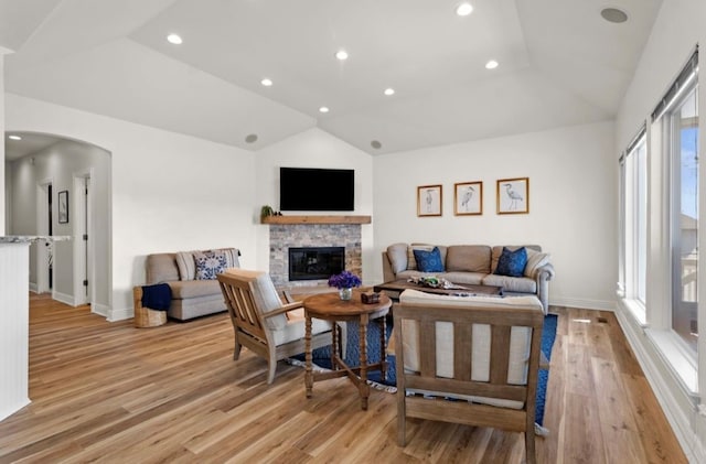 living room featuring light wood-type flooring, recessed lighting, arched walkways, a fireplace, and vaulted ceiling