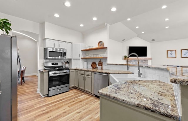 kitchen with light stone counters, a sink, stainless steel appliances, arched walkways, and decorative backsplash