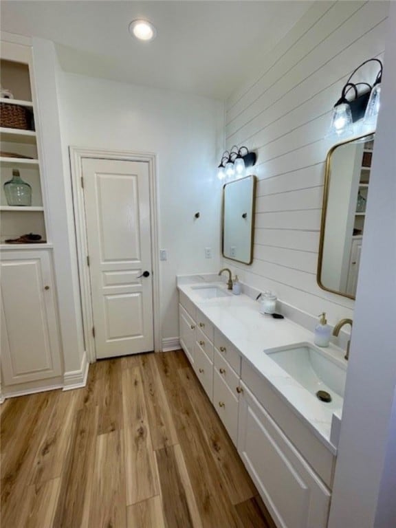 bathroom with a sink, wooden walls, wood finished floors, and double vanity