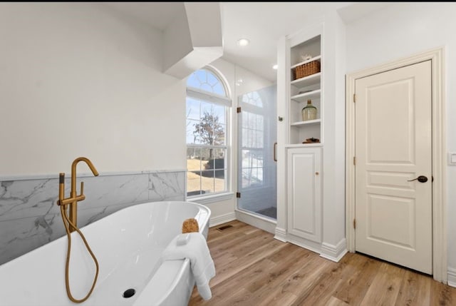 bathroom featuring visible vents, wood finished floors, tile walls, wainscoting, and a freestanding bath