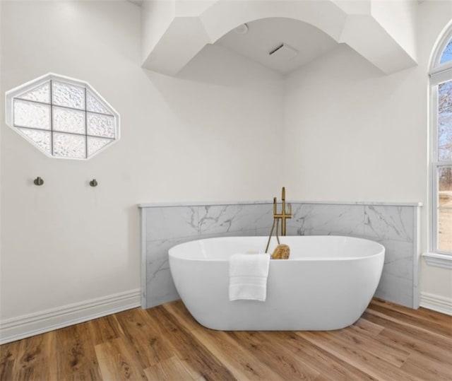 full bathroom with a soaking tub, tile walls, and wood finished floors