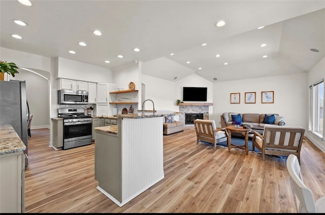 kitchen with light stone countertops, appliances with stainless steel finishes, a peninsula, and light wood finished floors